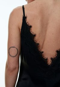Schwarzes ärmelloses Kleidungsstück mit einem tiefen V-Ausschnitt am Rücken, verziert mit zarter Spitze entlang der Kanten. Glatte, glänzende Textur mit taillierter Form.