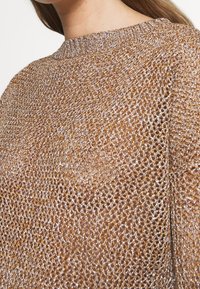 Pull en tricot à mailles semi-transparentes, composé de fils dorés et argentés, avec un col rond et une coupe décontractée.