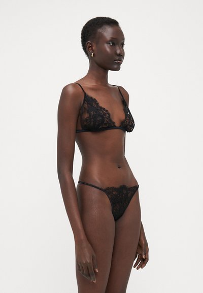 Zwarte kant lingerie set met intricat bloemenpatronen. Beha heeft verstelbare schouderbandjes; slip heeft dunne zijkanten en een transparante achterkant.
