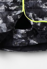 Jacket s černým a šedým vzorem s texturovaným povrchem, vybavený neonově zeleným zipem a zacvakávacími uzávěry na spodní části. Hladká saténová podšívka.