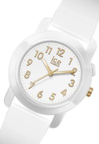Montre en silicone blanche avec un boîtier rond, index horaires dorés et aiguilles sur un cadran blanc. Logo doré positionné au-dessus du 6. Couronne décorative.