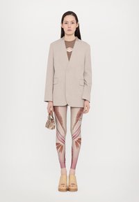 Beige blazer, brown cutout top, patterned leggings in pink tones, and wooden platform shoes. Holding a small floral bag.