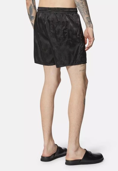 Shorts de bain noirs avec une taille élastique, dotés d'une poche arrière et d'une texture subtile, portés avec des sandales à glisser noires.