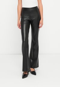 Pantalons évasés en simili cuir noir avec une texture lisse et une taille haute, associés à des escarpins noirs à bouts pointus.