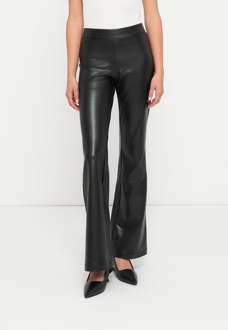 Pantalons évasés en simili cuir noir avec une texture lisse et une taille haute, associés à des escarpins noirs à bouts pointus.