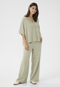 Gaiši zaļš, lielgabarīta krekls ar V-veida kakla izgriezumu, saskaņots ar platām biksēm. Mīksta tekstūra, vienkāršs dizains un bez redzamām rakstzīmēm.