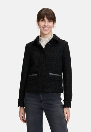 Zwarte gestructureerde jas met een kraag, twee voorzakken en zilveren accenten. Heeft een knoopsluiting en onafgewerkte randen. Draag met een licht shirt.