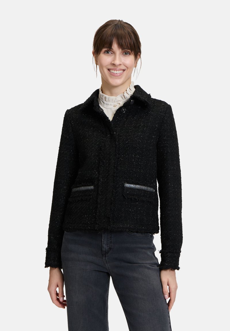 Czarna, fakturowana kurtka z kołnierzem, dwiema przednimi kieszeniami i srebrnymi akcentami. Posiada zapięcie na guziki oraz postrzępione krawędzie. Noszona z jasną koszulą.