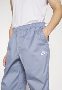 Pantaloni jogger azzurri realizzati in tessuto leggero, con vita elastica e tasche laterali, dotati di un logo Nike bianco sulla coscia sinistra.