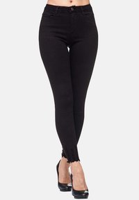 Jean skinny noir en denim, avec une taille haute et un ourlet effiloché. Associés à des chaussures à talons hauts noires.