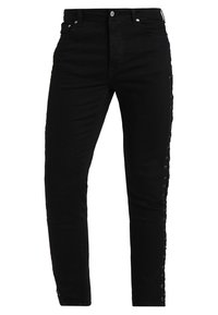 Jeans de mezclilla negra con un corte ajustado, que presentan detalles de cordones a lo largo de los lados y un diseño clásico de cinco bolsillos.