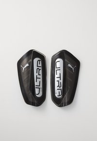 Puma Ultra Flex scheenbeschermers, zwarte kunststof met zilveren accenten, hebben een gestroomlijnde vorm en een gestructureerd oppervlak voor flexibiliteit en bescherming.