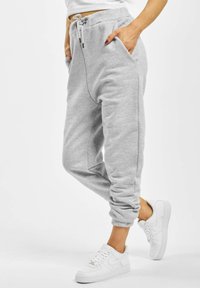Un pantalon de survêtement gris avec une taille élastique à cordon de serrage, des poches latérales et des poignets resserrés, associé à des baskets blanches, mettant en avant une coupe décontractée et confortable.