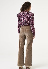 Bloes met bloemenpatroon en ruches, zwarte achtergrond, roze en paarse accenten; gecombineerd met lichtbruine corduroy wijde broek.