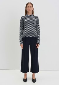 Schwarz-weißer karierter Strickpullover kombiniert mit hoch taillierten, weiten Marineblauen Hosen und schwarzen spitzen Schuhen. Minimalistisches Design.