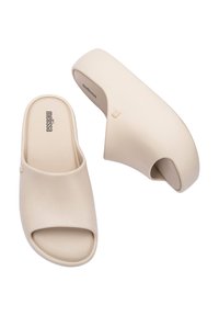 Mule platform in beige realizzati in materiale sintetico, caratterizzati da punta aperta, finitura liscia e una leggera curvatura nel design del tacco. Nome del marchio "melissa" visibile.