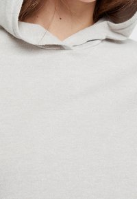 Vaaleanharmaa huppari, jossa on pehmeä, ribattu pinta. Suunnittelussa on huppu, jossa on yksinkertainen kaula-aukko. Ei näkyviä kuvioita tai yksityiskohtia.