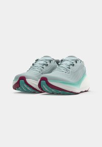 Une paire de chaussures de running bleu clair avec des semelles intermédiaires blanches, des accents turquoise et des semelles extérieures marron sur un fond blanc uni.