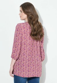 Blomstret skjorte med lange ærmer i nuancer af lyserød med en løs pasform, med en rygfæld og et mønster designet med små hvide og lilla blomster.