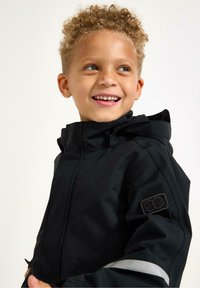 Černá voděodolná bunda s kapucí, s reflexní páskou, hladkou texturou a logem na rukávu. Model dítěte se usmívá.