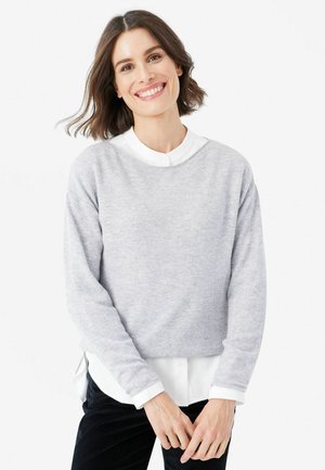 Light gray, soft-textured, cropped sweater with long sleeves, worn over a white collared shirt; features a relaxed neckline and side slits.