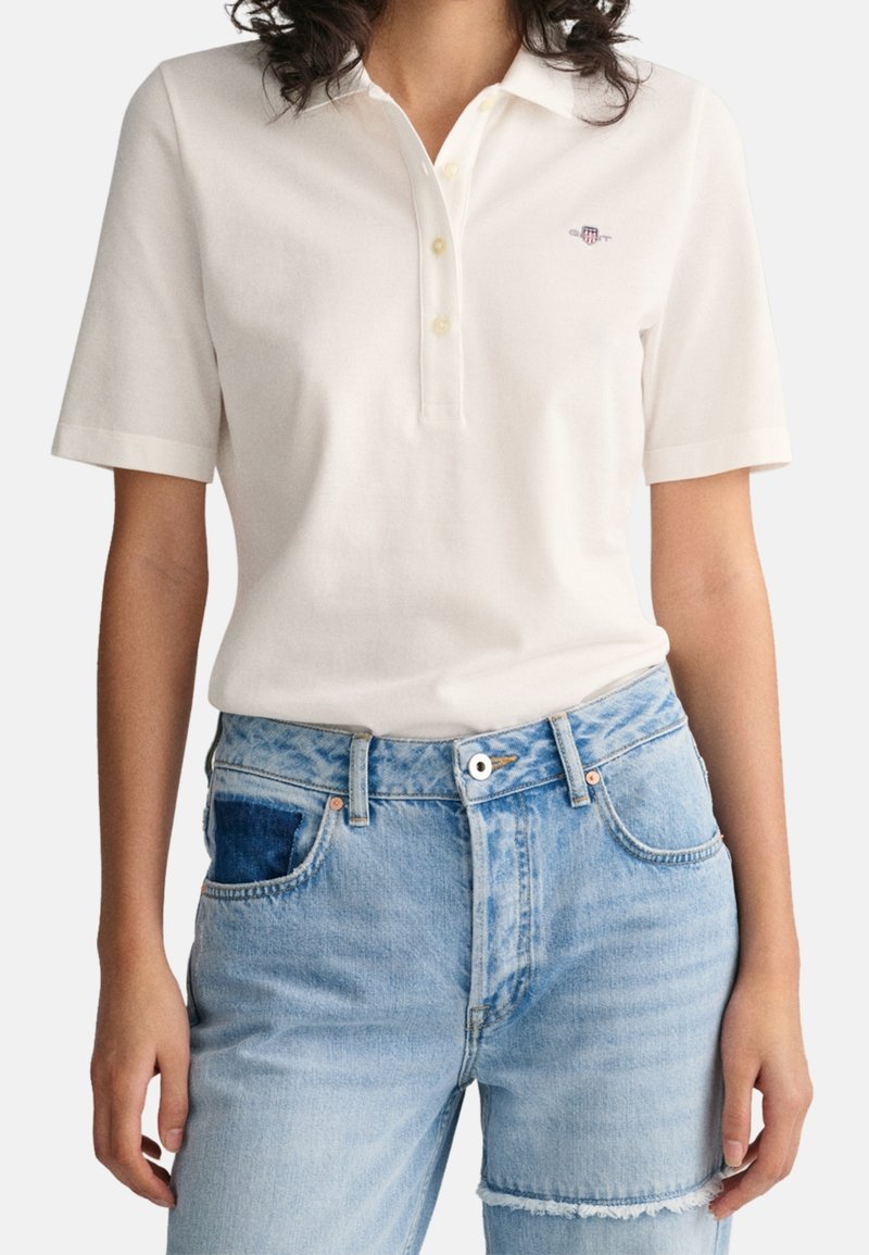 Hvid polo-shirt med korte ærmer, tre-knaps placket og lille logo på brystet. Matcher med lyseblå slidte denim jeans.