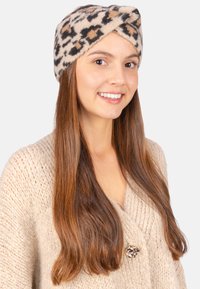 Bandeau turban en tricot à imprimé léopard dans des tons beige, marron et noir. Texture douce avec un design torsadé, porté avec un pull en tricot de couleur crème.