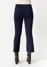 Pantaloni sartoriali blu navy con tessuto elasticizzato, design aderente, orli svasati e due tasche posteriori. Abbinati a stivali neri con tacco.