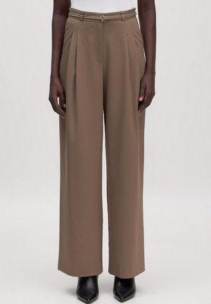 Hoch taillierte, weit geschnittene Taupe-Hose mit Falten und schmalem Gürtel, kombiniert mit schwarzen spitzen Stiefeletten und einem weißen Oberteil.