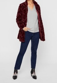 Bordowy płaszcz z sztucznego futra o luźnym kroju, noszony na jasnoszary sweter z dekoltem w serek oraz ciemnoniebieskie jeansy proste, połączony z czarnymi botkami z ogniowymi detalami.