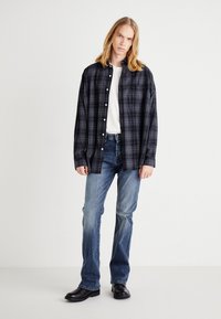 Camisa de xadrez preta e azul-marinho com mangas longas e fecho de botão, combinada com jeans azul-claro e sapatos pretos. Design simples e casual.