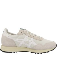 Zapato deportivo beige con una combinación de malla y ante. Detalles en blanco, cordones redondos y una suela texturizada. Diseño clásico de running.