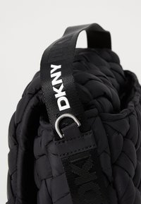Borsa imbottita nera con una texture intrecciata, dotata di una tracolla brandizzata nera con lettering bianco e un anello in argento.