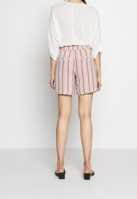 Pruhované šortky s elastickým pasem, primárně červené a bílé. V kombinaci se volným bílým topem, nošeny s sandály na blokovém podpatku.