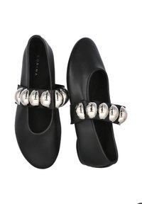 Zapatos de cuero negro con puntera redondeada, que presentan una amplia correa adornada con esferas metálicas plateadas en la parte frontal.