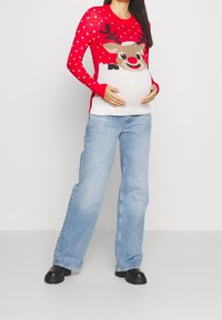 Rode gebreide trui met witte stippen en een rendierontwerp, gecombineerd met lichtblauwe wijde jeans en zwarte chunky laarzen.
