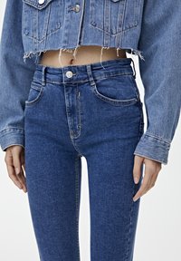 Jeans de denim azul de talle alto con una silueta ajustada, que cuentan con un diseño de cinco bolsillos y costuras en contraste a lo largo de las costuras.