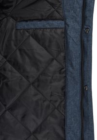 Gequilte, donkere zwarte voering met een getextureerde blauwe stof aan de buitenkant en een functionele zijzak, voorzien van een rits- en knoopsluiting.