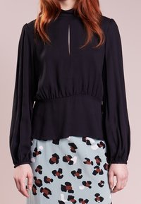 Svart långärmad topp med hög halsringning och nyckelhål, matchad med en mönstrad kjol med ljusblå, svarta och bruna accenter.