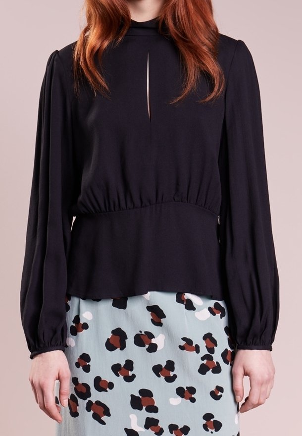 Svart långärmad topp med hög halsringning och nyckelhål, matchad med en mönstrad kjol med ljusblå, svarta och bruna accenter.