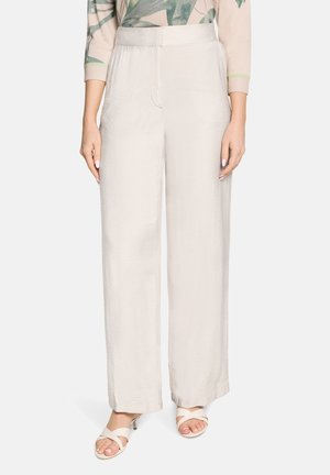 Pantalon large en satin beige clair porté avec des talons ouverts et un haut à manches longues à imprimé de feuilles vertes.