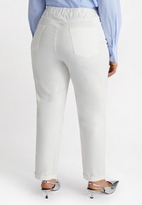 Witte, elastische taillebroek met een rechte pijp, voorzien van twee achterzakken en een omslagonderkant, gecombineerd met zilveren hoge hakken.