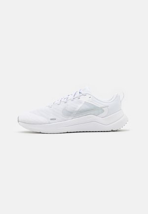 Biały lekki sportowy sneaker z siateczkową cholewką, jasnoszarym logo Nike, amortyzowaną podeszwą i zapięciem na sznurowadła, pokazany z profilu.