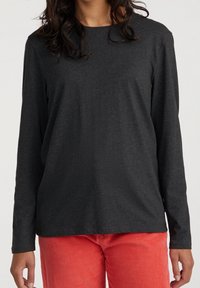 Schwarzes Langarmshirt aus weichem Stoff, runder Ausschnitt, lockere Passform. Kombiniert mit roten Baumwollhosen aus Cord mit vertikaler Rippstruktur.