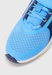 Baskets de sport bleu clair avec tige en mesh, superpositions texturées et accents marine. Comprend un système de laçage et un logo de marque visible.
