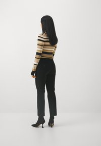 Haut à manches longues rayé en beige, noir et doré ; associé à un pantalon noir et des escarpins ; tissu texturé avec une coupe ajustée.