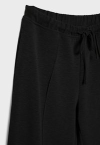 Schwarze Jogginghose aus weichem Material. Sie hat einen elastischen Bund mit Kordelzug, Seitentaschen und einen lockeren Schnitt.