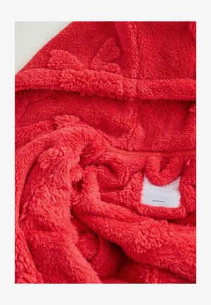 Červená, plyšová deka s kapucňou a mäkkým, textúrovaným povrchom. Obsahuje štítok vo vnútri. Materiál sa zdá byť chlpatej a útulnej textúry, vhodný na zahriatie.