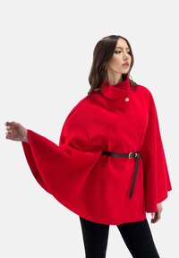 Cappotto stile mantello di tessuto testurizzato. Presenta un colletto alto, chiusura con un bottone singolo e una cintura nera in vita.