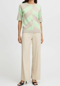 Pull à manches courtes vert menthe et beige à motif géométrique, associé à un pantalon beige à jambes larges et à des sandales noires à talons. Texture lisse.